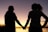 Two people hold hands against a scenic sunset backdrop. Their silhouettes are clearly defined as they face each other, suggesting a moment of connection and intimacy.