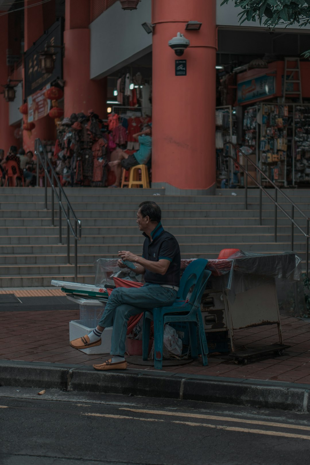 man in blue t-shirt sitting on blue plastic chair reading newspaper