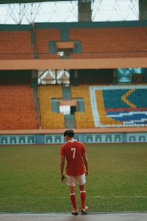 man in red jersey shirt standing on green grass field during daytime
