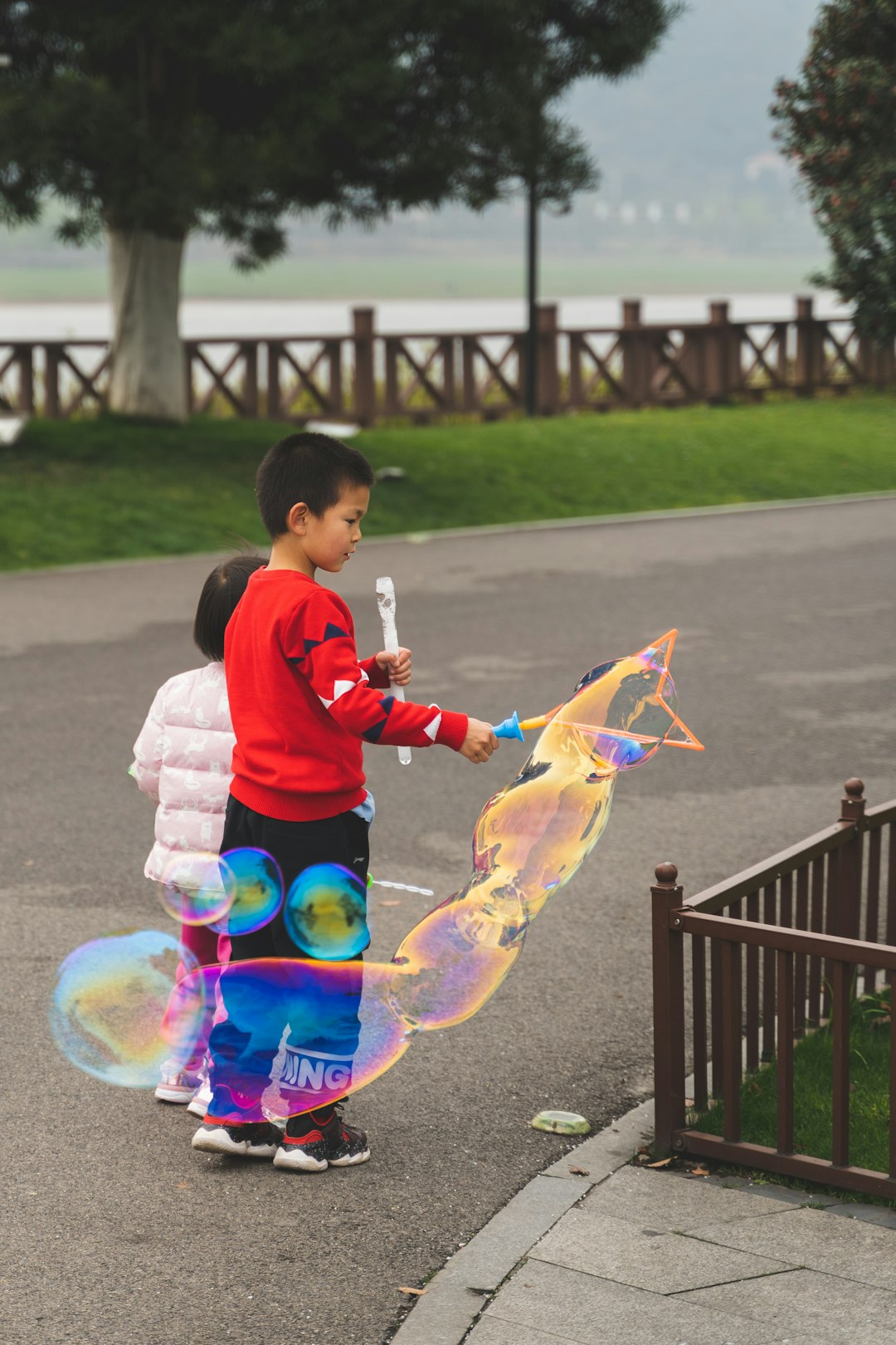 girl in white and pink jacket playing bubbles during daytime