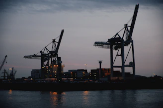 Container cranes operating at dusk with a backdrop of a busy European port terminal.