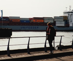 woman in red jacket standing on black metal railings near body of water during daytime