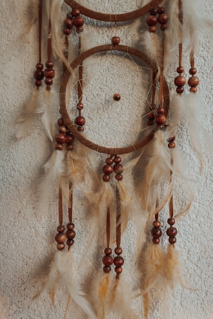 A dreamcatcher with wooden beads and soft, light-colored feathers hanging against a textured wall.
