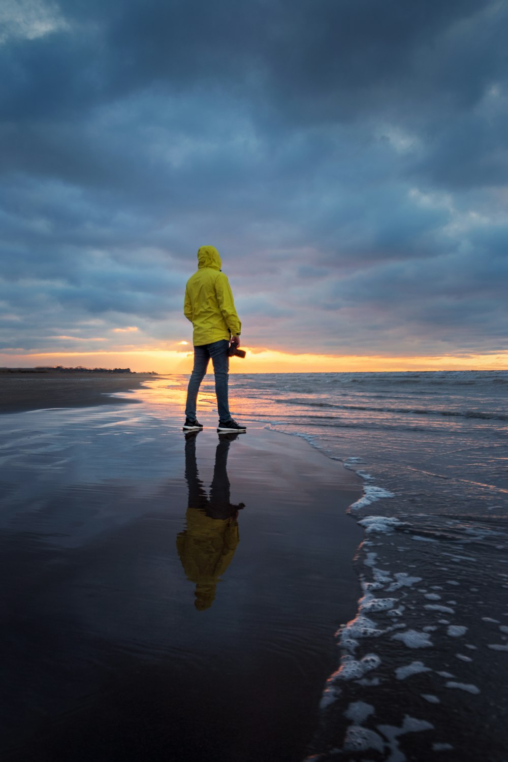 Person in gelbem Kapuzenpulli, die tagsüber am Meeresufer steht