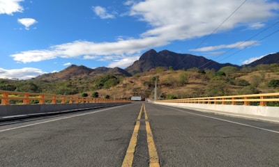 gray concrete road near green mountains under blue sky during daytime