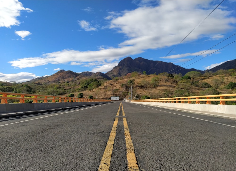 estrada de concreto cinza perto de montanhas verdes sob o céu azul durante o dia