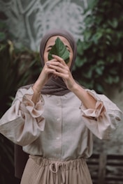 woman in white button up shirt covering her face with white and green textile