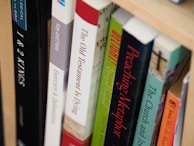A close-up view of books arranged on a wooden shelf, with titles focusing on theological and religious themes. The spines of the books display various colors and fonts, suggesting a scholarly collection.