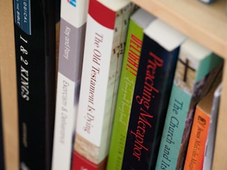 A close-up view of books arranged on a wooden shelf, with titles focusing on theological and religious themes. The spines of the books display various colors and fonts, suggesting a scholarly collection.