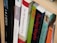 A close-up view of books arranged on a wooden shelf, with titles focusing on theological and religious themes. The spines of the books display various colors and fonts, suggesting a scholarly collection.