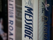 A row of books on a shelf focuses on the spine of a book titled 'The Message'. The titles of other books are partially visible, providing a sense of a personal library or a collection.