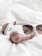 A pair of rose gold and white over-ear headphones is placed on a soft, white fabric. Beside the headphones, there is a pair of stylish sunglasses with tinted lenses. The arrangement suggests a casual and relaxed atmosphere.