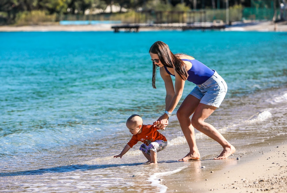 Foto mujer en camiseta sin mangas azul y blanca sosteniendo a bebé en  onesie blanco en la playa durante el día – Imagen Familia gratis en Unsplash