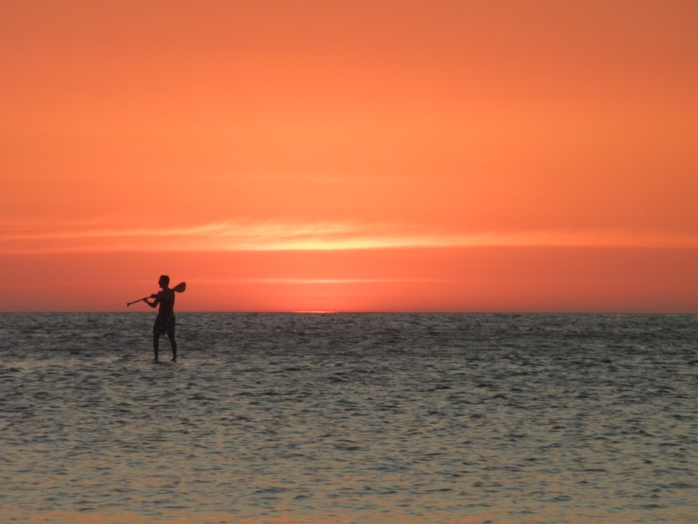 man in black shorts standing on sea shore during sunset