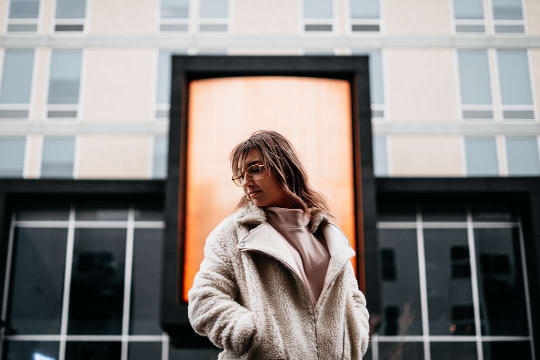 woman in beige coat standing near glass window during daytime