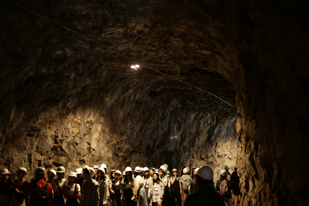 Underground mining workers wearing protective gear inspecting heavy metal mining equipment in a dimly lit tunnel.