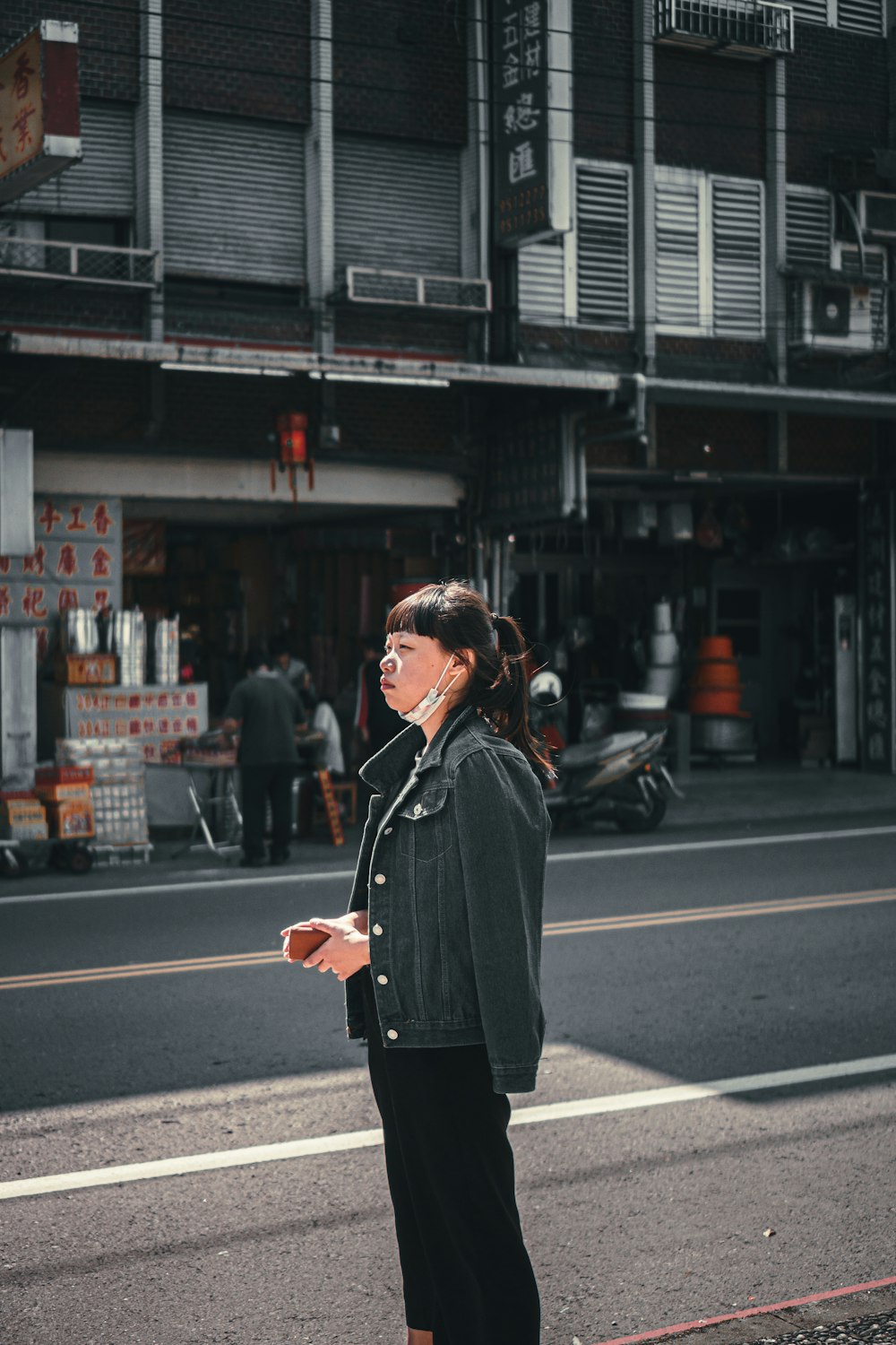 woman in black coat standing on sidewalk during daytime