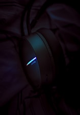 A close-up of a headphone with a glowing light strip, showcasing a spectrum of colors in a dimly lit environment. The focus is on the light, creating a moody contrast against the dark background.