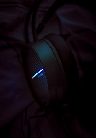 Close-up of glowing neon headphones resting on a black surface with gold accents reflecting nearby lights.