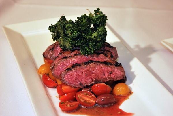 Sliced meat with sliced tomatoes and green vegetable on white ceramic plate