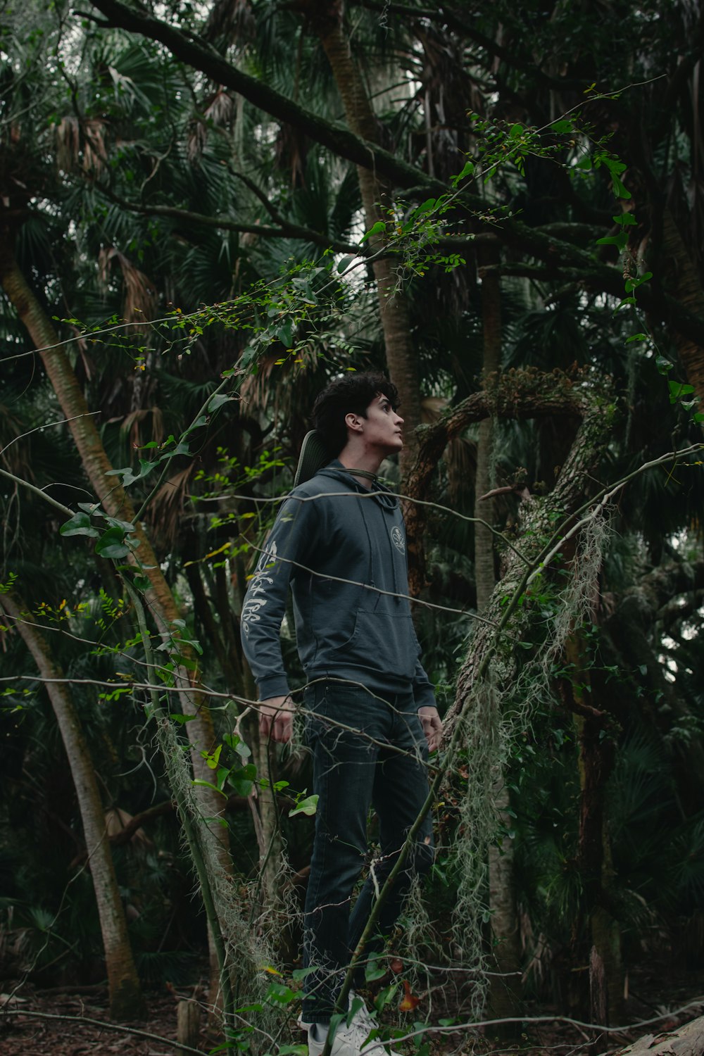 Mann in grauem Kapuzenpulli, der tagsüber in der Nähe grüner Bäume steht