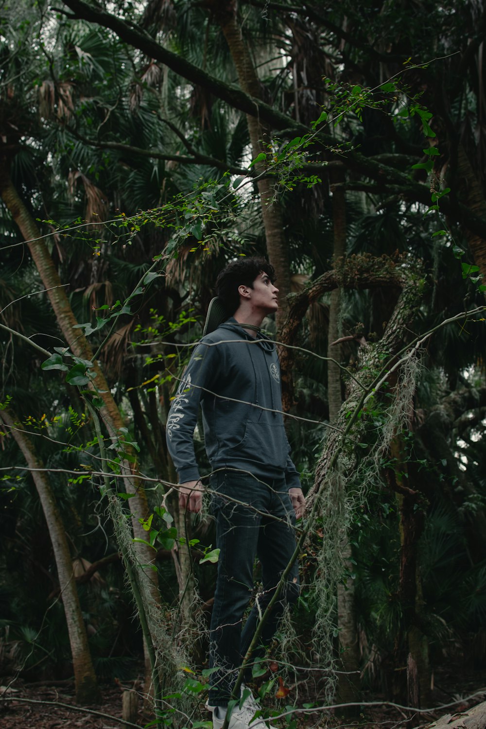 man in gray hoodie standing near green trees during daytime