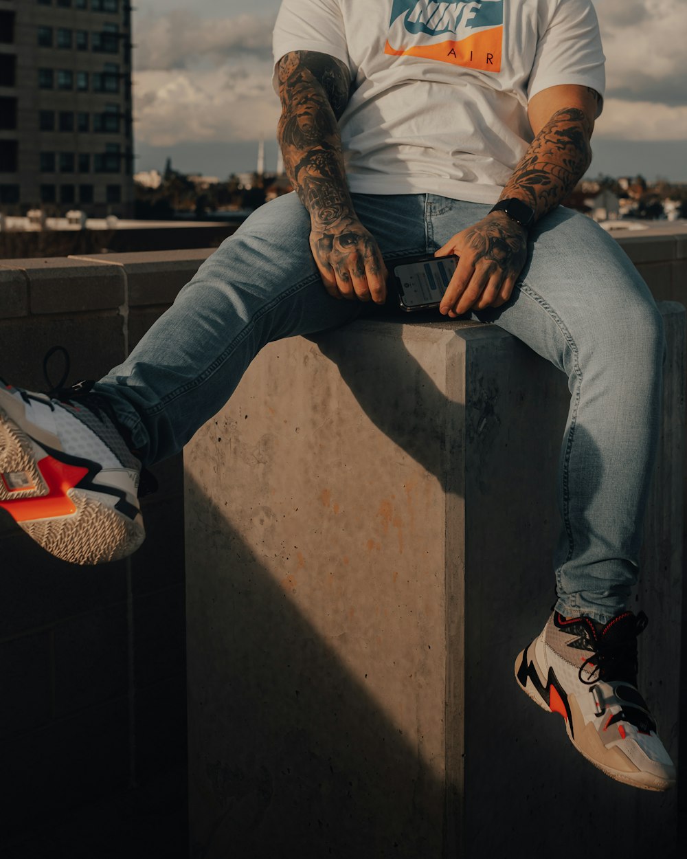 man in white shirt and blue denim jeans sitting on concrete wall