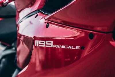 A close-up view of a red motorcycle showcasing the logo '1199 Panigale R' on its side. The surface appears glossy with reflections, emphasizing the bike's sleek and aerodynamic design.
