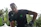A determined young man executing a swift boxing move outdoors with lush greenery behind.