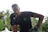 A determined young man executing a swift boxing move outdoors with lush greenery behind.