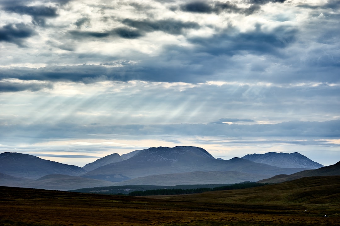 green grass field near mountains under white clouds during daytime