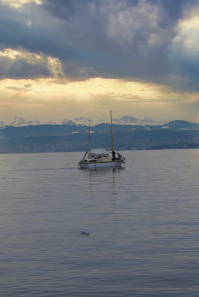 A sailboat cutting through calm, glassy waters with towering icebergs in the background under a soft pastel sky.