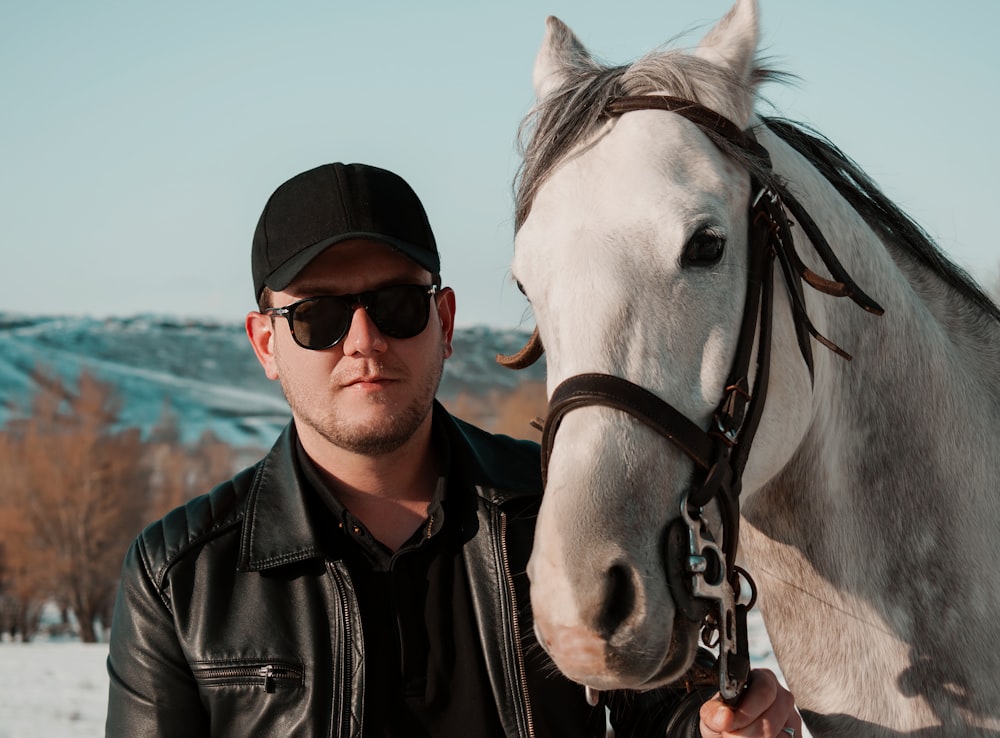 man in black leather jacket standing beside white horse during daytime