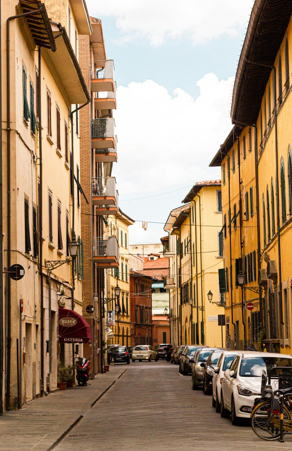 cars parked on side of the road in between buildings during daytime