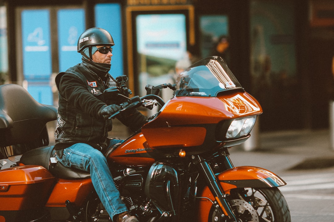 man in black leather jacket and blue denim jeans riding orange and black motorcycle