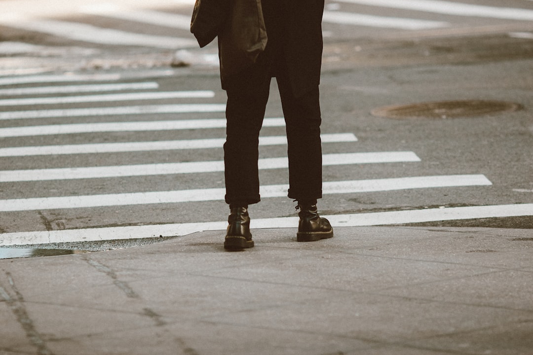 person in black pants and black boots standing on pedestrian lane during daytime