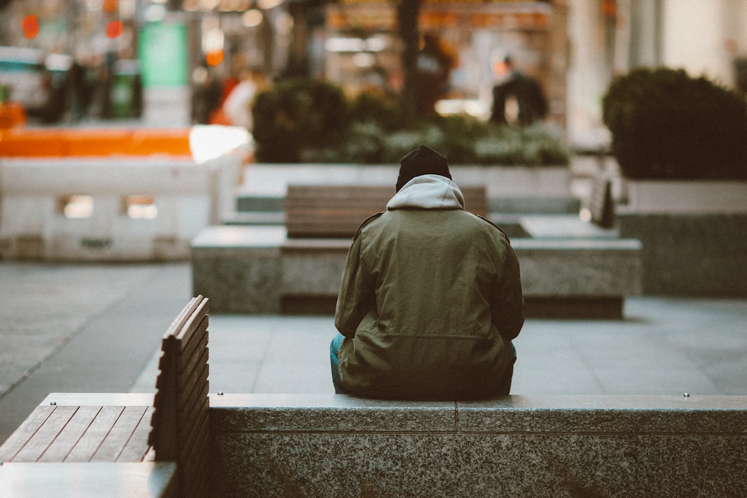 person in gray hoodie sitting on gray concrete bench during daytime