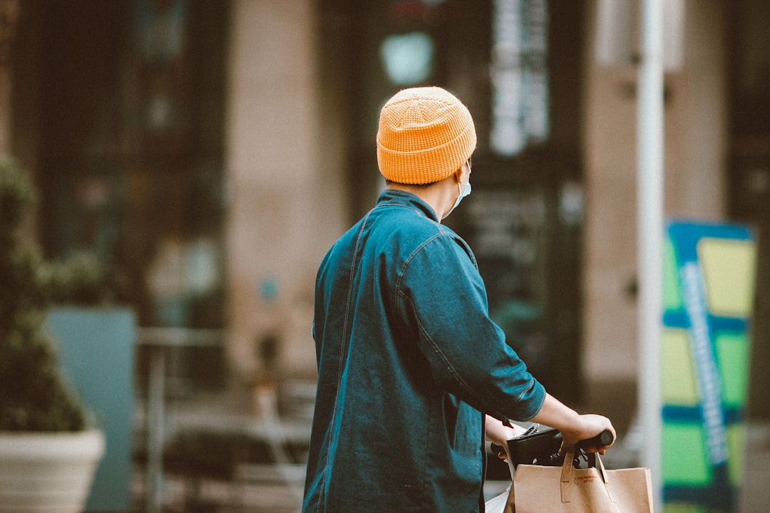 person in blue jacket wearing orange knit cap standing near black bicycle during daytime