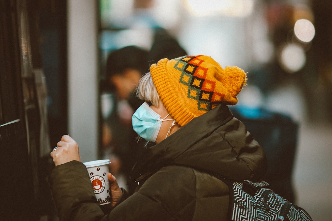 person in yellow knit cap and black jacket holding white ceramic mug