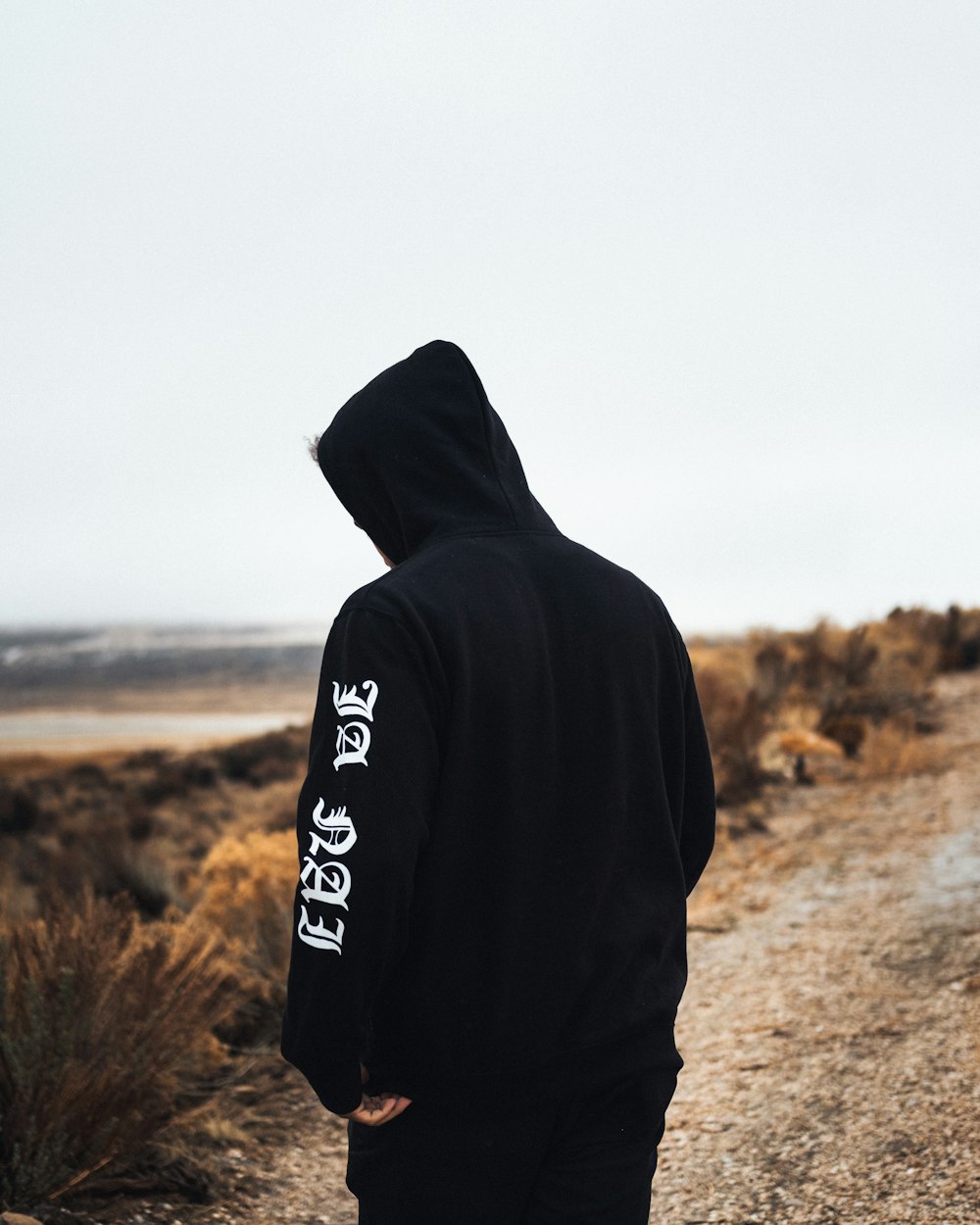 personne en sweat à capuche noir et blanc debout sur un champ brun pendant la journée