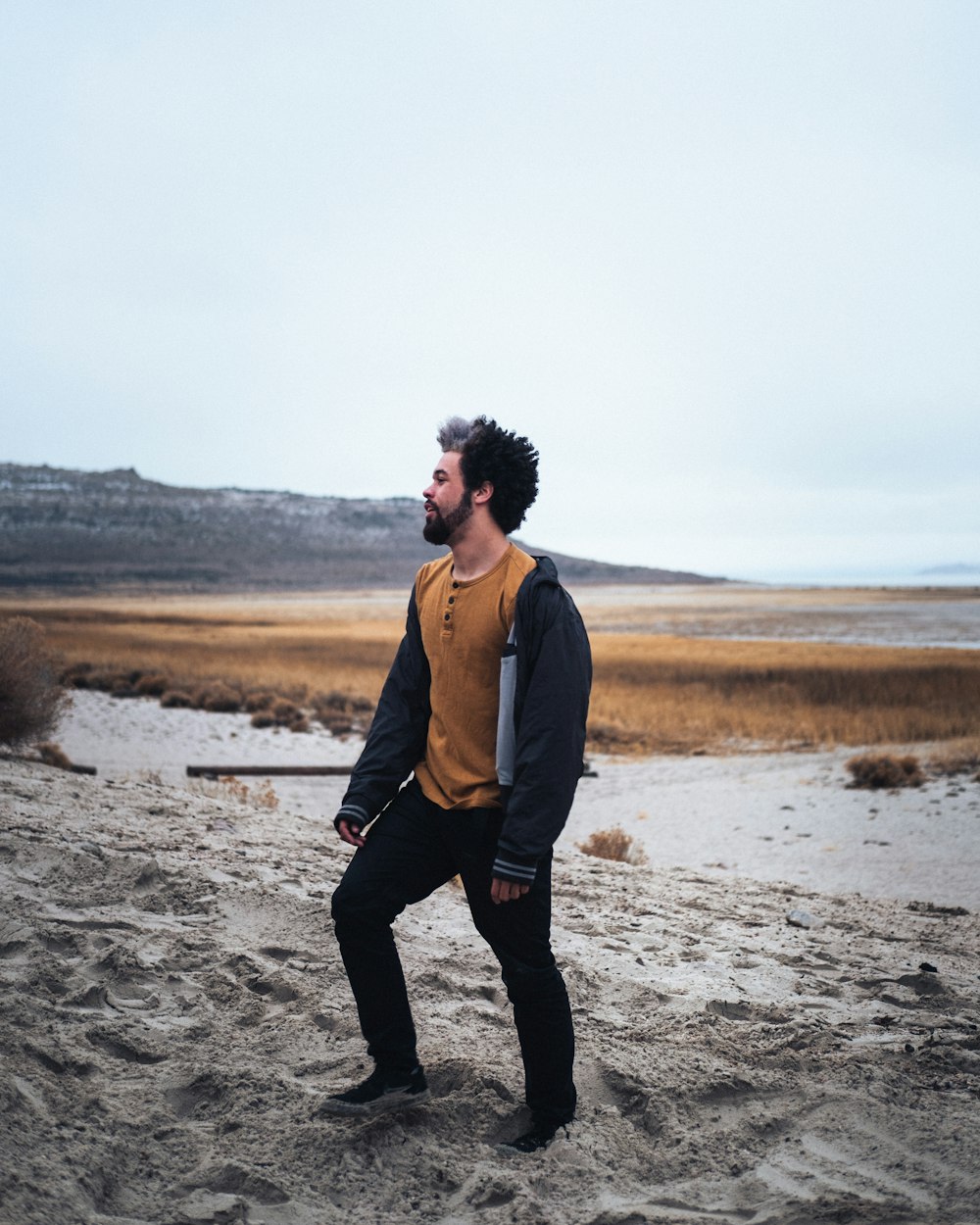 man in brown jacket and black pants standing on gray sand during daytime