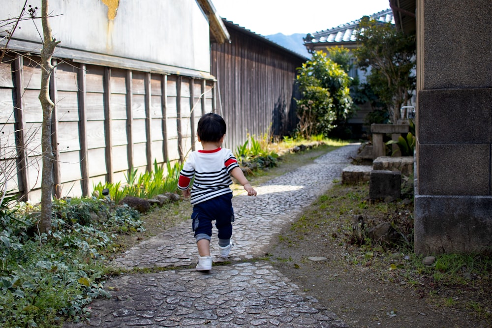 boy in black and white stripe t-shirt and black shorts standing on gray concrete pathway