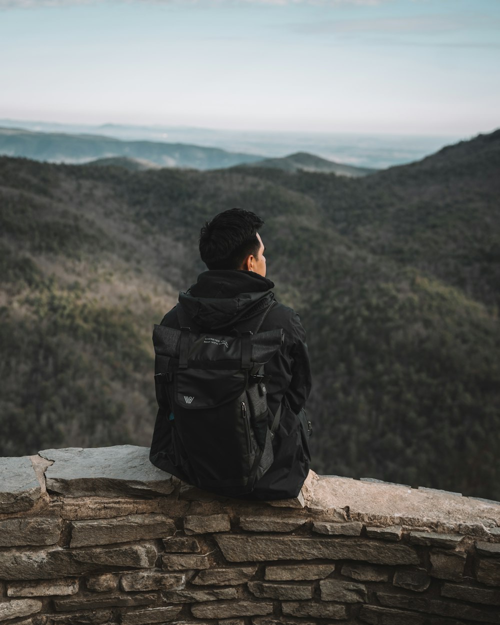 man in black jacket sitting on rock during daytime