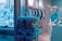 A store display features a mannequin wearing a bunny mask and a turquoise T-shirt, seated near a teal vending machine. The background includes hanging shirts in various colors, mostly white and turquoise. Neon blue signage is on the wall, contributing to a vibrant, modern atmosphere.