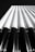 A monochromatic architectural image featuring a series of vertical, cylindrical structures that appear to be part of a building facade. The perspective is from below, looking up towards the sky, emphasizing the height and linearity of the design.
