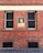 A red brick wall with two windows, one of which has a vintage-style monochromatic poster of a person with 'AUSSIE' written beneath it.