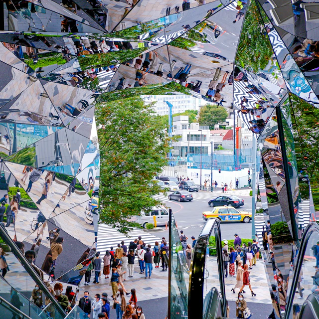 Pedestrians crossing near the mirrored entrance of Tokyu Plaza Omotesando Harajuku in Tokyo