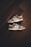 A pair of brown and white sneakers with prominent branding positioned on a dark wooden floor. The stylish shoes have a low-top design with white shoelaces and a distinctive swoosh logo on the sides.