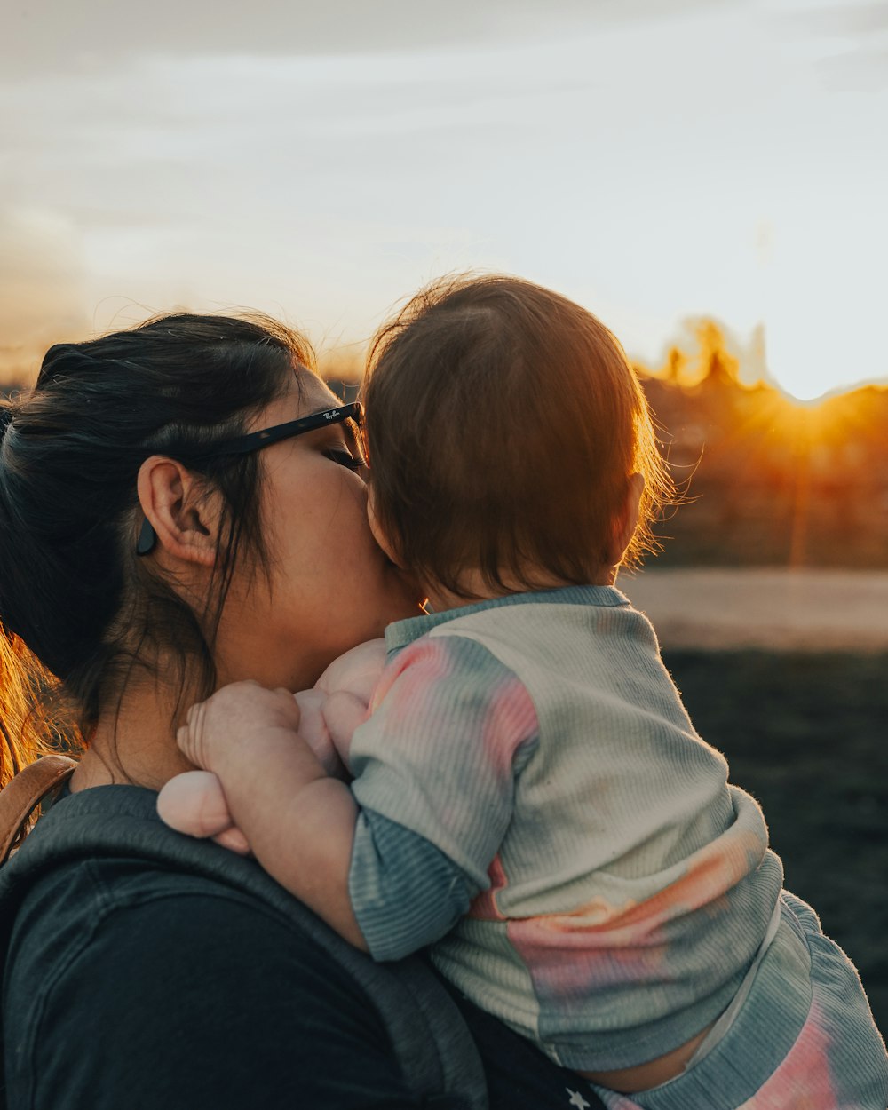 woman in black shirt carrying baby in white and pink jacket during sunset