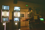 People intensely focused on their dart throws, with sports events visible on the large TV screens behind them.